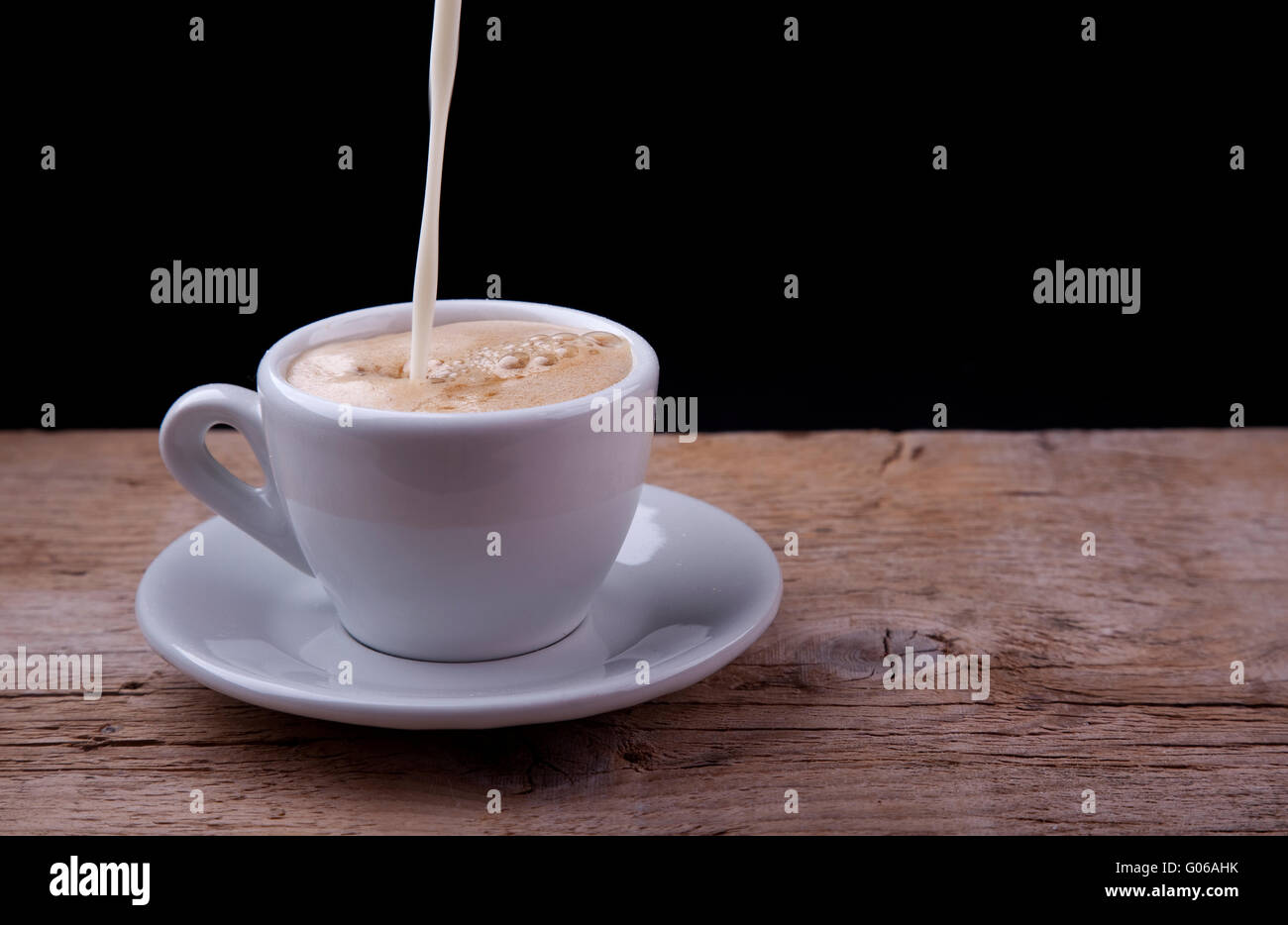 Café avec du lait qui se déverse sur la table en bois Banque D'Images