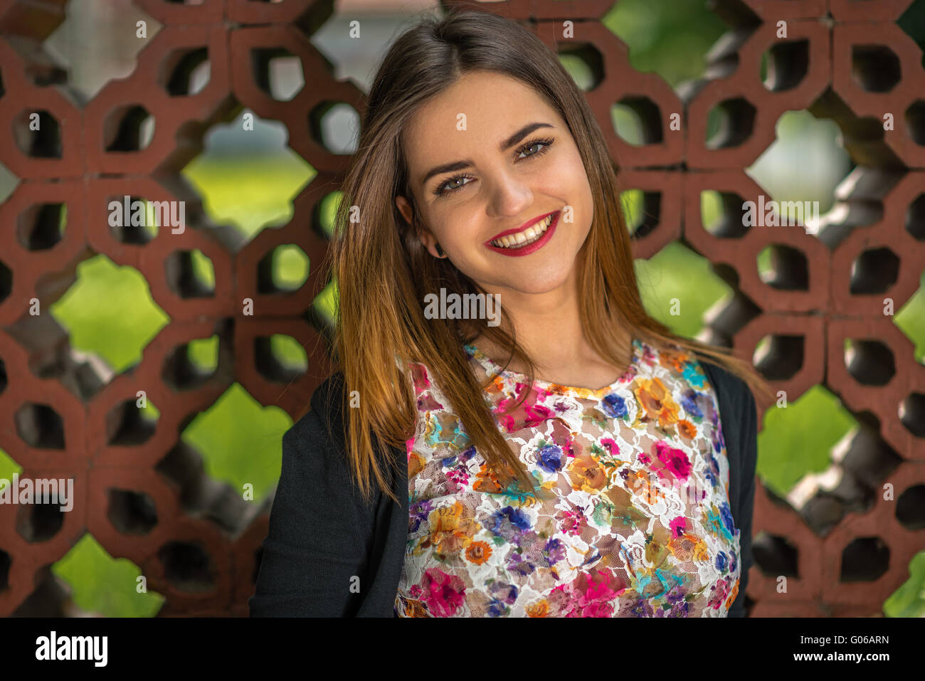Portrait d'une belle jeune femme avec un grand sourire, les yeux brillants et les lèvres rouge contre une clôture faite de briques d'ornement. Shallo Banque D'Images