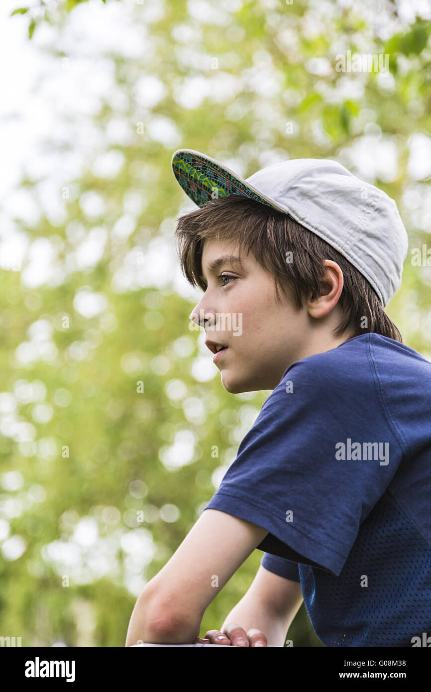 Profil d'un jeune garçon avec basecap et feuilles vertes floues en arrière-plan Banque D'Images