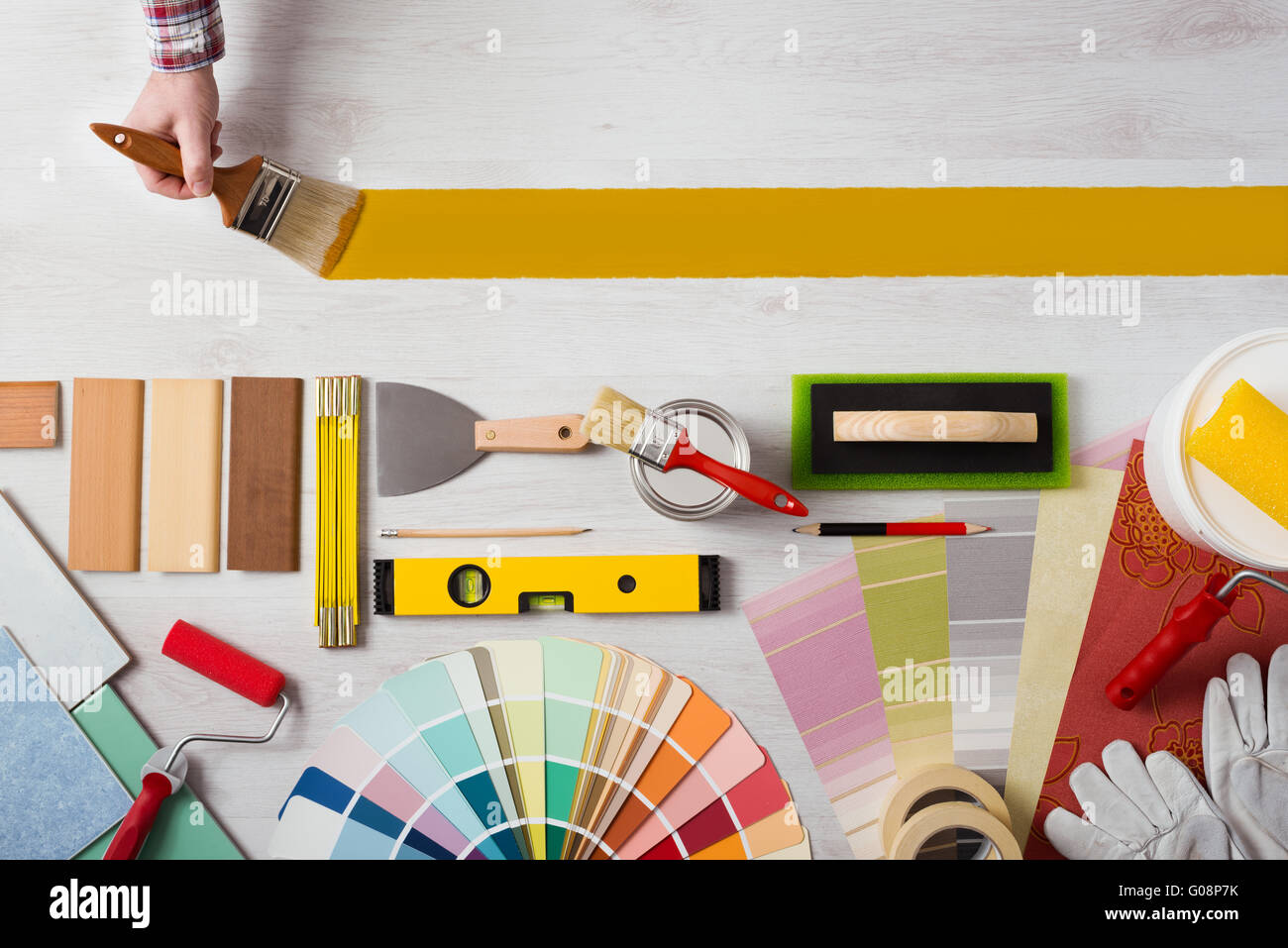 La tenue d'un décorateur le pinceau et peindre une surface en bois, outils de travail et des échantillons au fond, bannière avec copie espace Banque D'Images