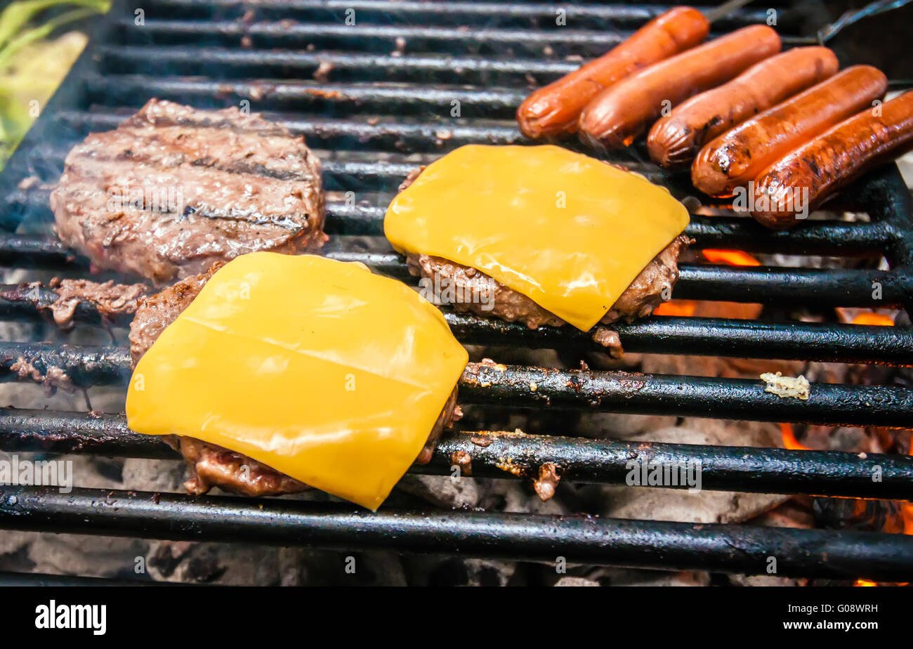 Des hamburgers avec du fromage et des hot-dogs sur la calandre Banque D'Images