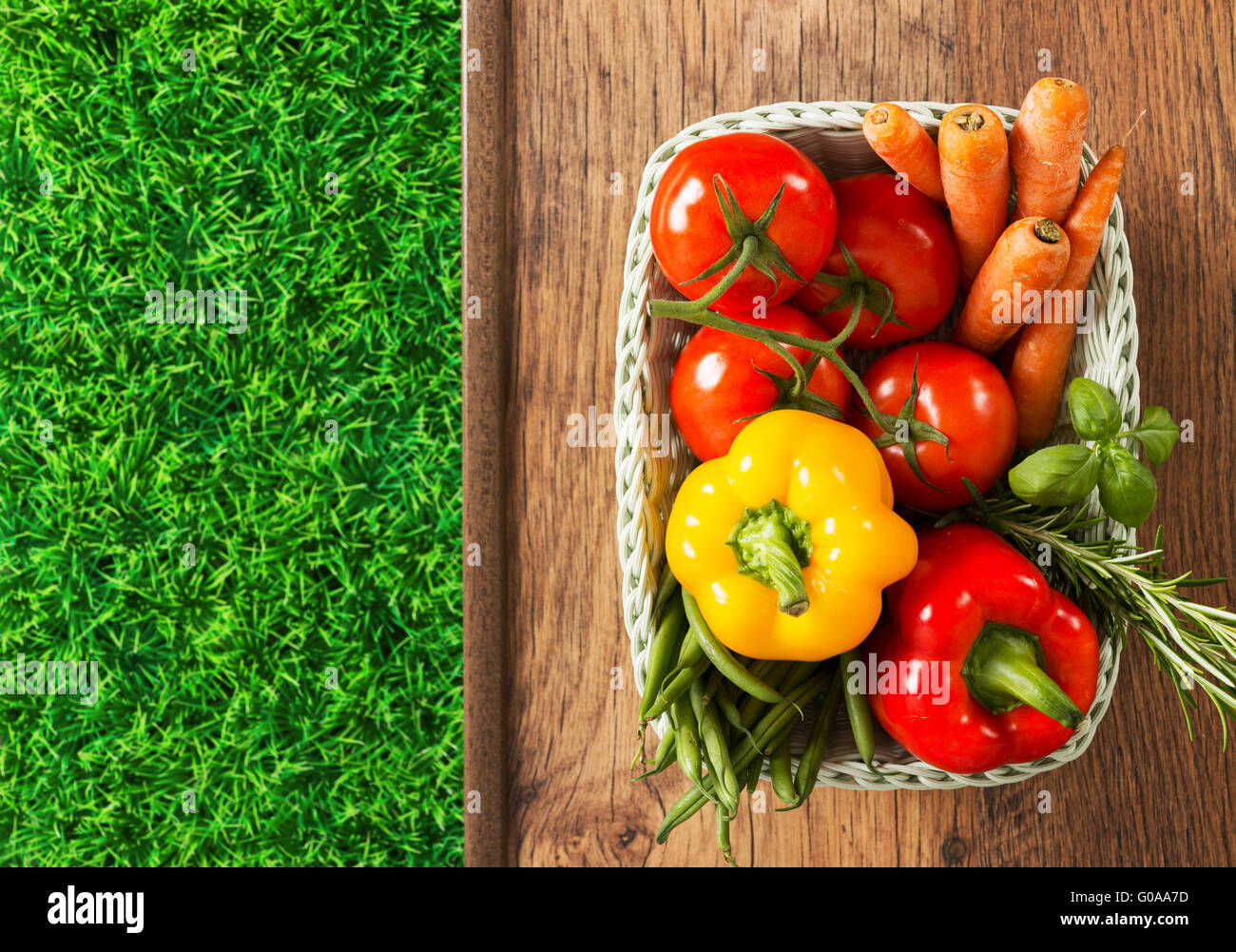 Les légumes fraîchement récoltés et des herbes dans un panier blanc et vert gazon sur une table en bois Banque D'Images