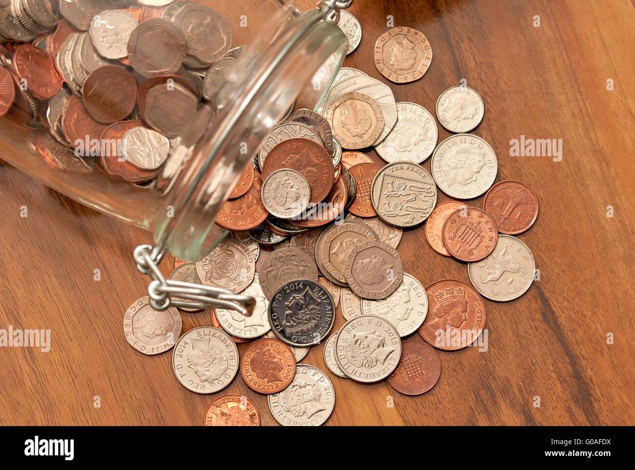 L'épargne en verre bocal avec coins spilling out sur le plancher Banque D'Images