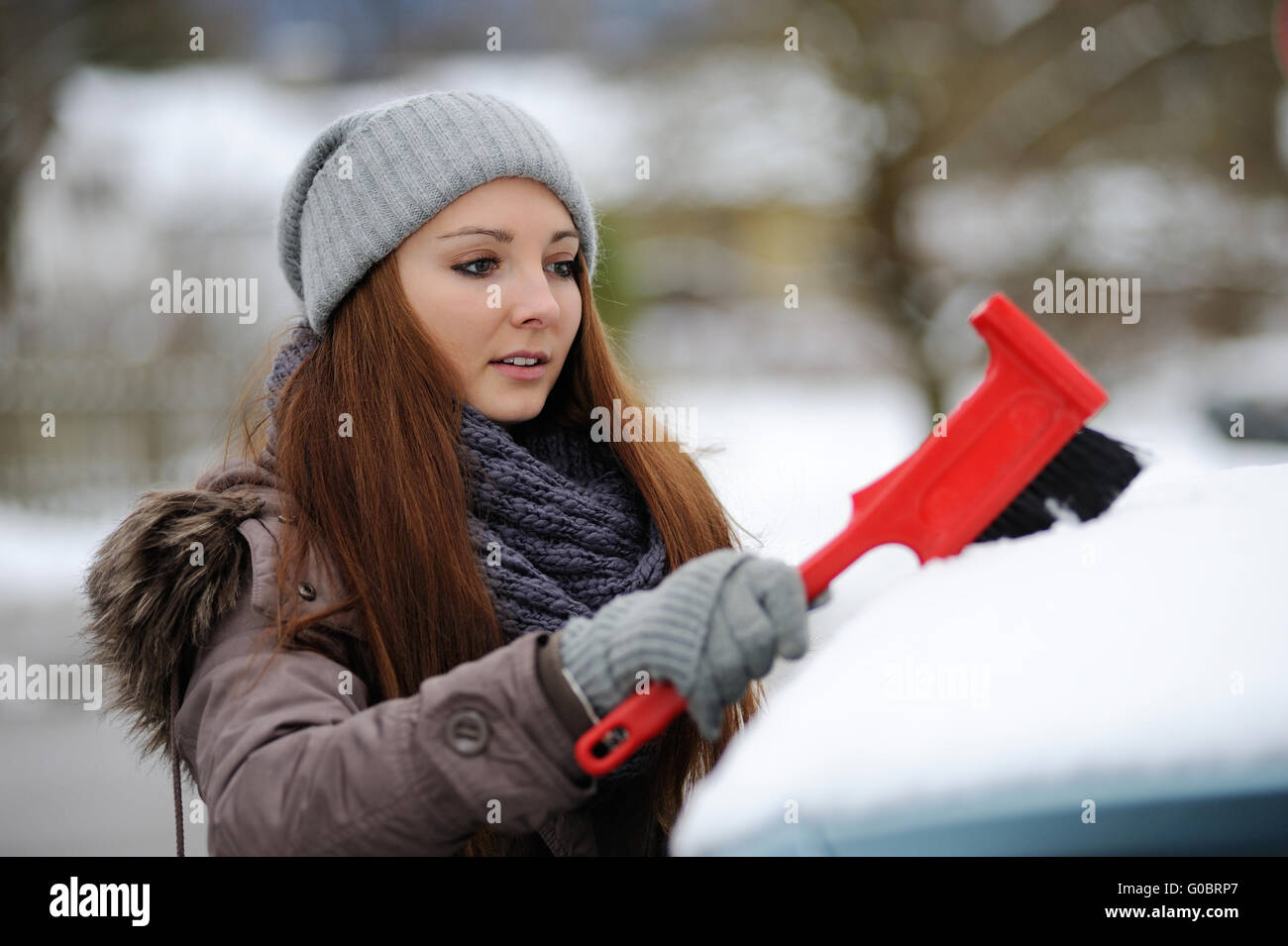 Jeune femme balaie la neige de sa voiture Banque D'Images