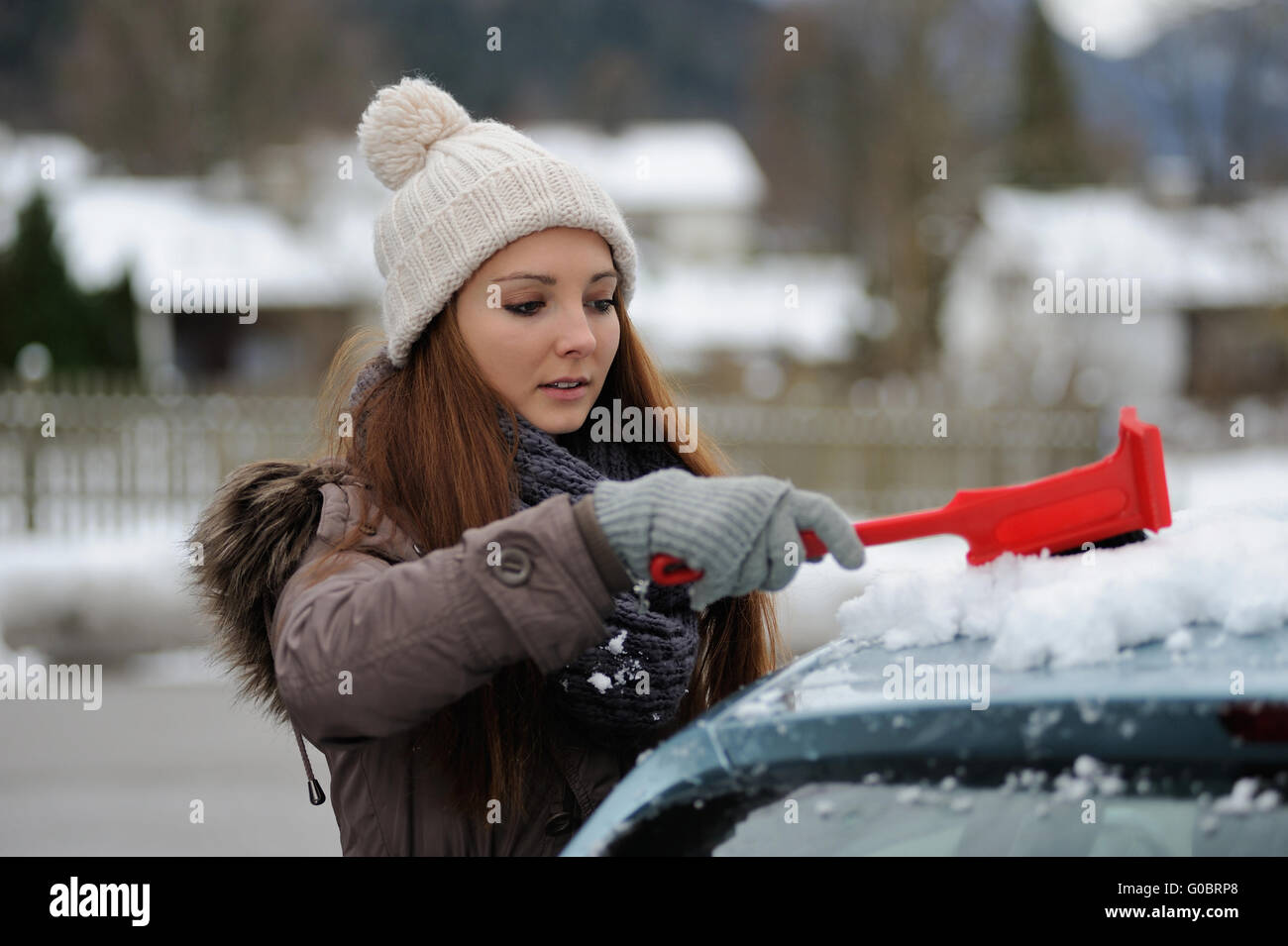 Jeune femme balaie la neige de sa voiture Banque D'Images