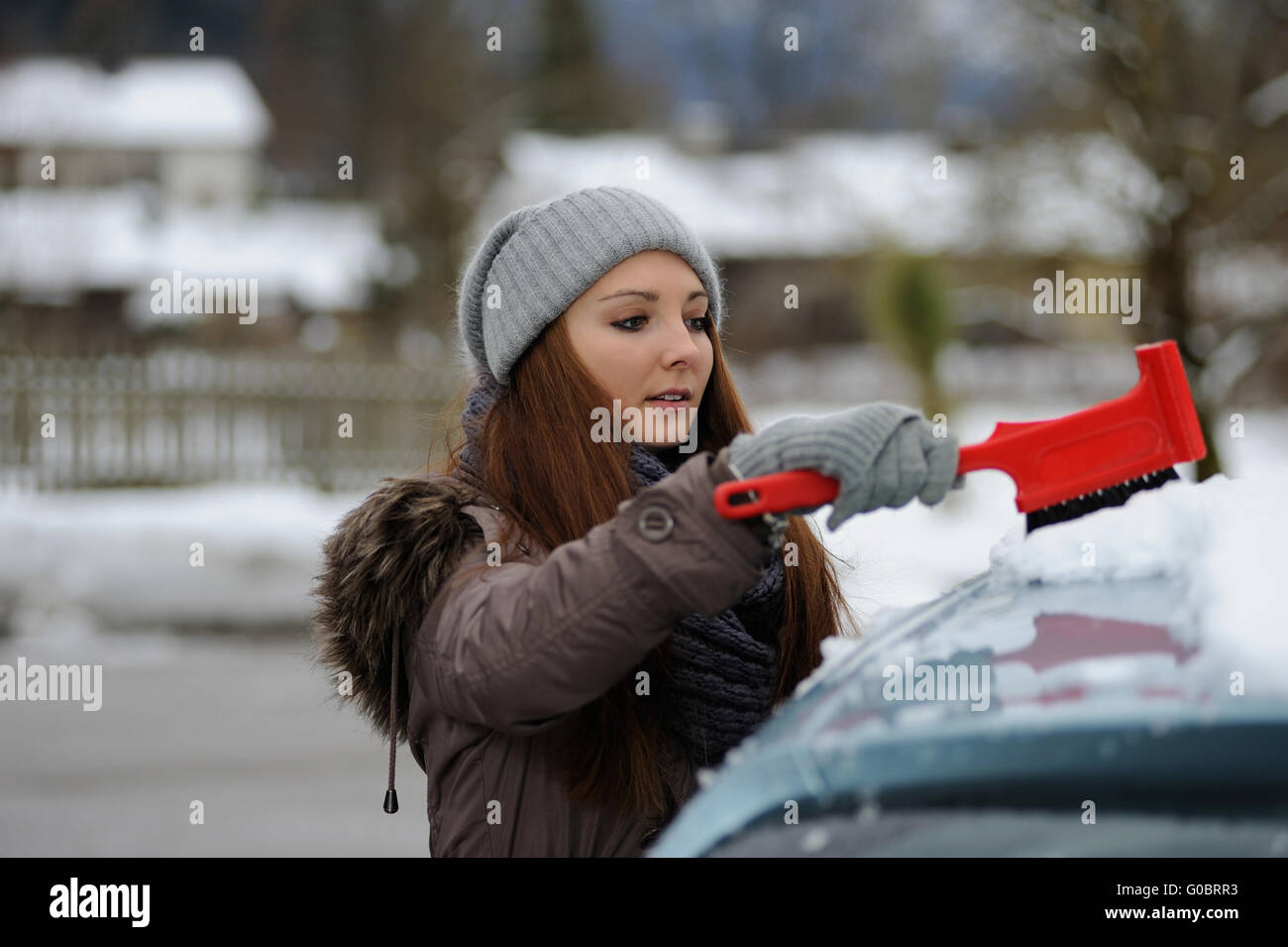 Jeune femme balaie la neige de sa voiture Banque D'Images