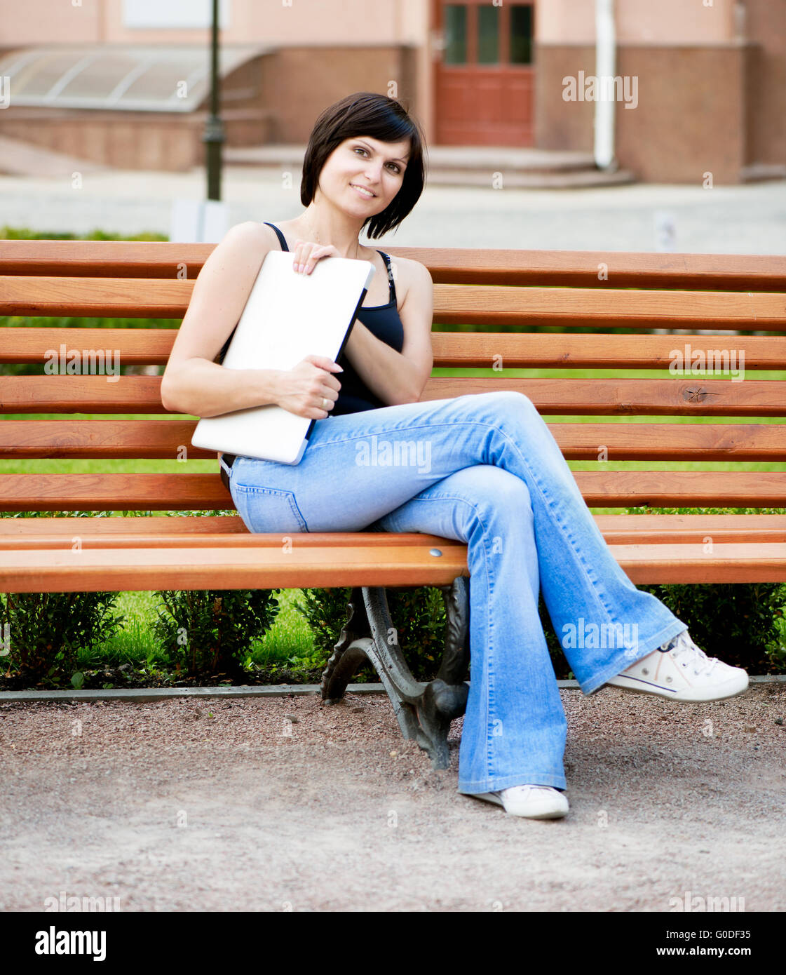 Fille brune assise sur une journée ensoleillée sur un banc dans le parc avec un ordinateur portable dans ses mains Banque D'Images