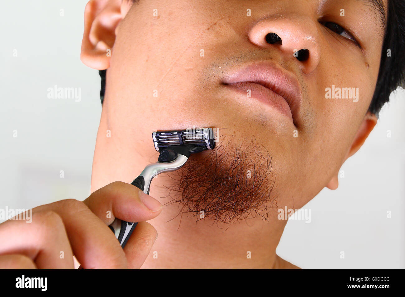 Young Asian man shaving ses cheveux du visage sans crème Banque D'Images