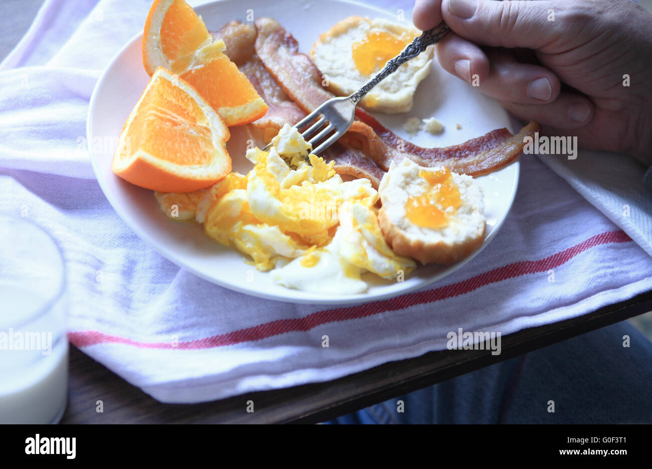 Un homme mange un copieux petit-déjeuner de bacon, oeufs brouillés, biscuit avec de la confiture et des quartiers d'orange. Banque D'Images