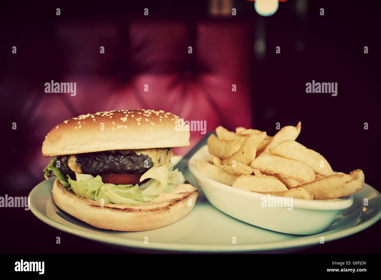 Délicieux hamburger et frites sur plaque dans american food restaurant. Canapé en cuir rouge à l'arrière-plan. Vintage Banque D'Images