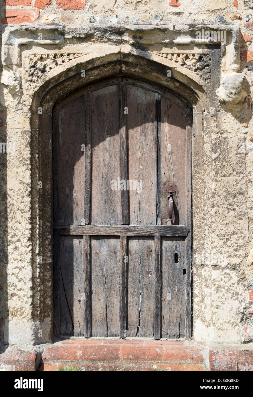Une vieille porte en bois, avec son surround de pierre dans le mur d'une église en Angleterre. Banque D'Images