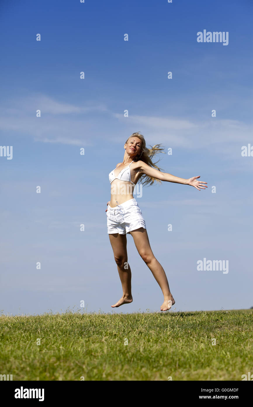 Le happy woman in bikini blanc et shorts les sauts dans un champ vert d'été Banque D'Images