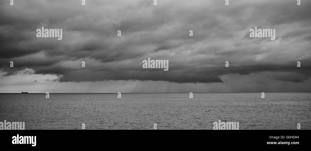 Grand porte-conteneurs à l'horizon la voile vers les nuages orageux très avec la pluie qui tombe Banque D'Images