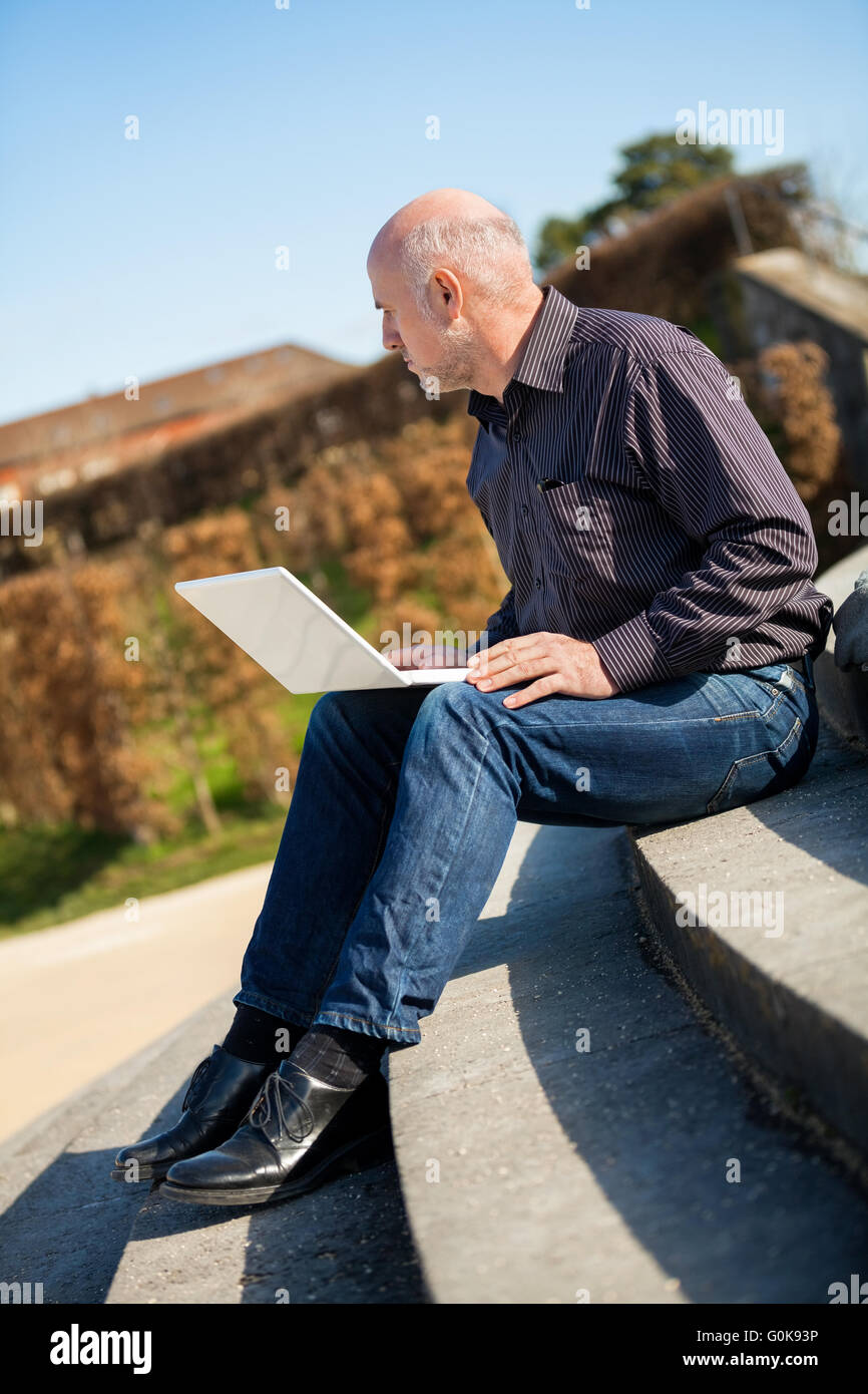 Homme assis sur un banc à l'aide d'un ordinateur portable Banque D'Images