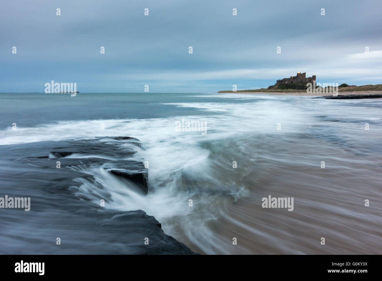 Le bruit de la mer comme il l'ebbs retour après une vague s'écraser sur la plage de Bamburgh et château de Bamburgh en arrière-plan. Banque D'Images