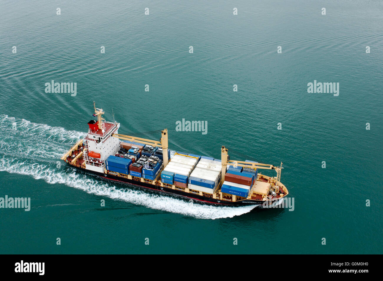 Porte-conteneurs le sud de Lily têtes hors de l'Auckland Harbour avec des conteneurs de transport et des voitures sur le pont. Banque D'Images