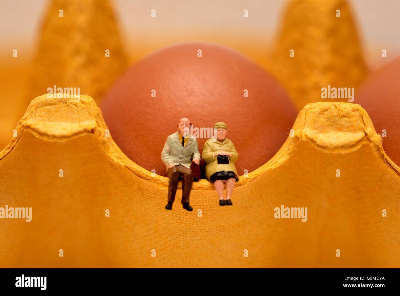 Un couple retraité figurine miniature assis sur un œuf située en face d'un oeuf Banque D'Images