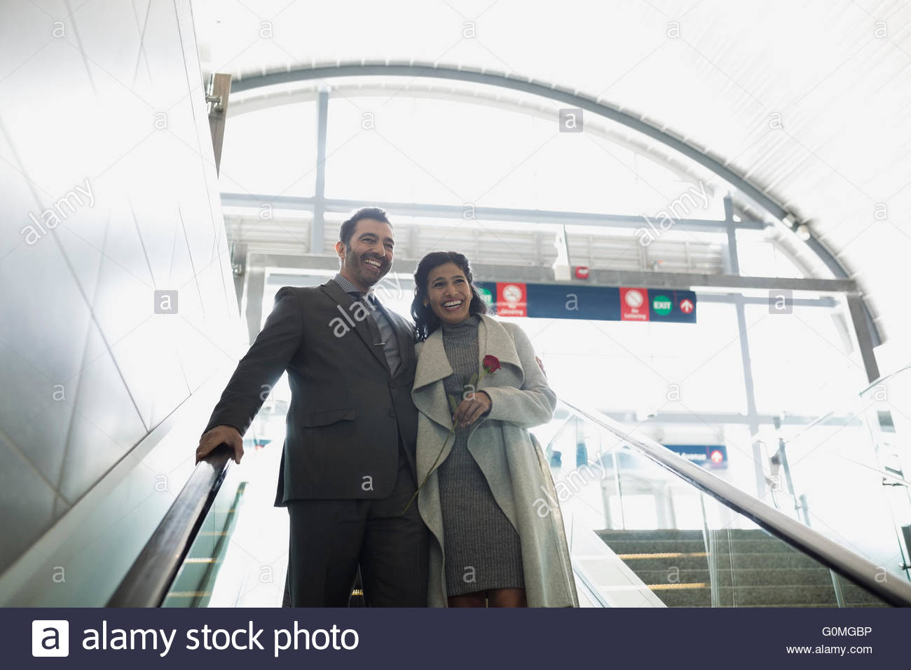 Smiling couple descending escalator at train station Banque D'Images