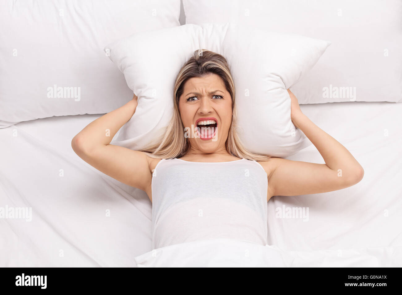 Femme furieuse couvrant ses oreilles avec un oreiller et essayer de dormir Banque D'Images