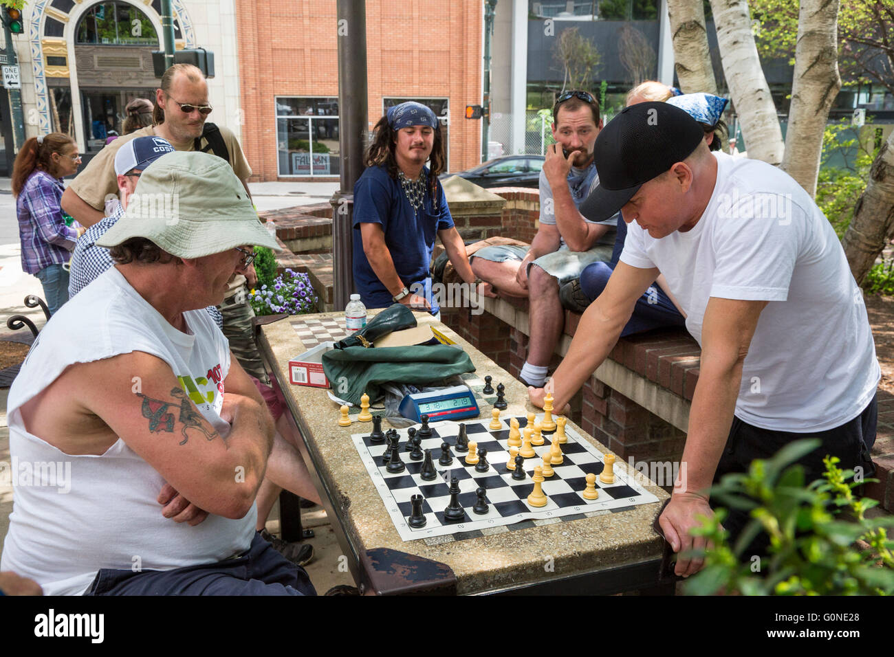 Asheville, Caroline du Nord - l'acteur Woody Harrelson (bouchon noir) joue aux échecs dans Pritchard Park. De nombreux habitués du parc sont sans abri. Banque D'Images