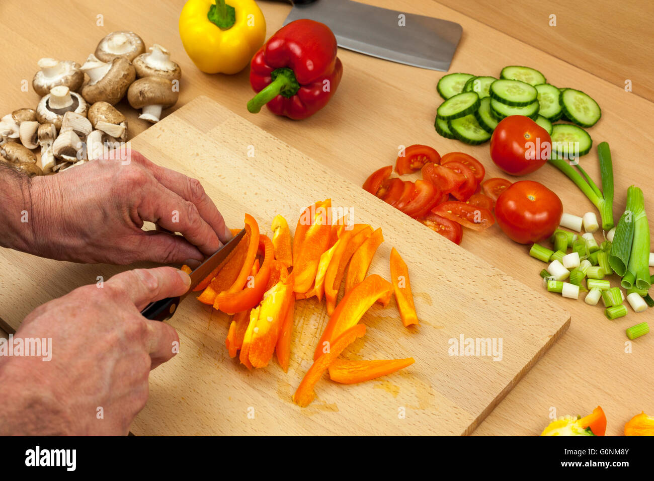 Gros plan d'un découpage des mains de chefs un poivron orange nettoyés sur une planche à découper en bois de côté une sélection de légumes hachés Banque D'Images