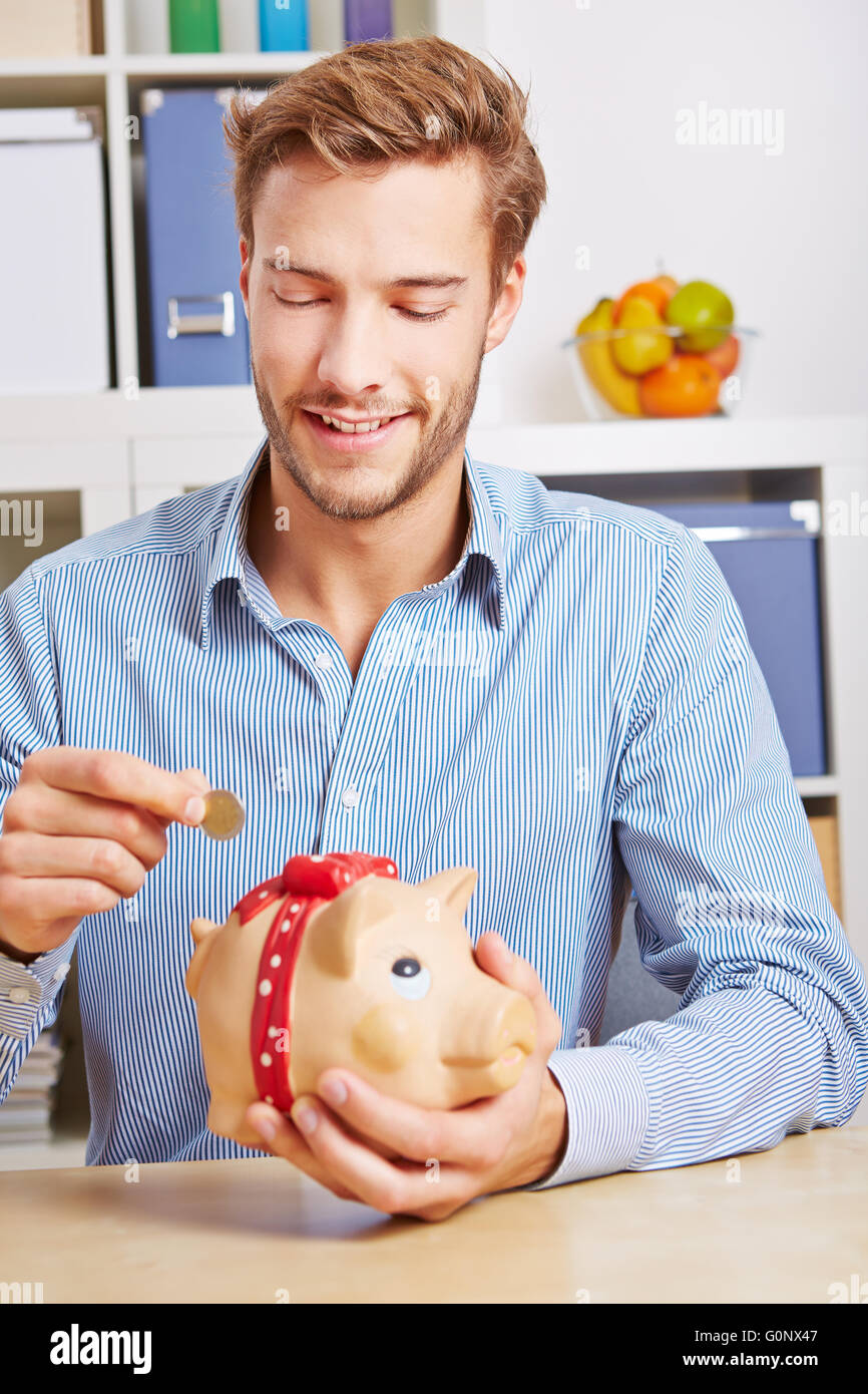 Jeune homme séduisant de mettre de l'argent Euro coins in piggy bank Banque D'Images