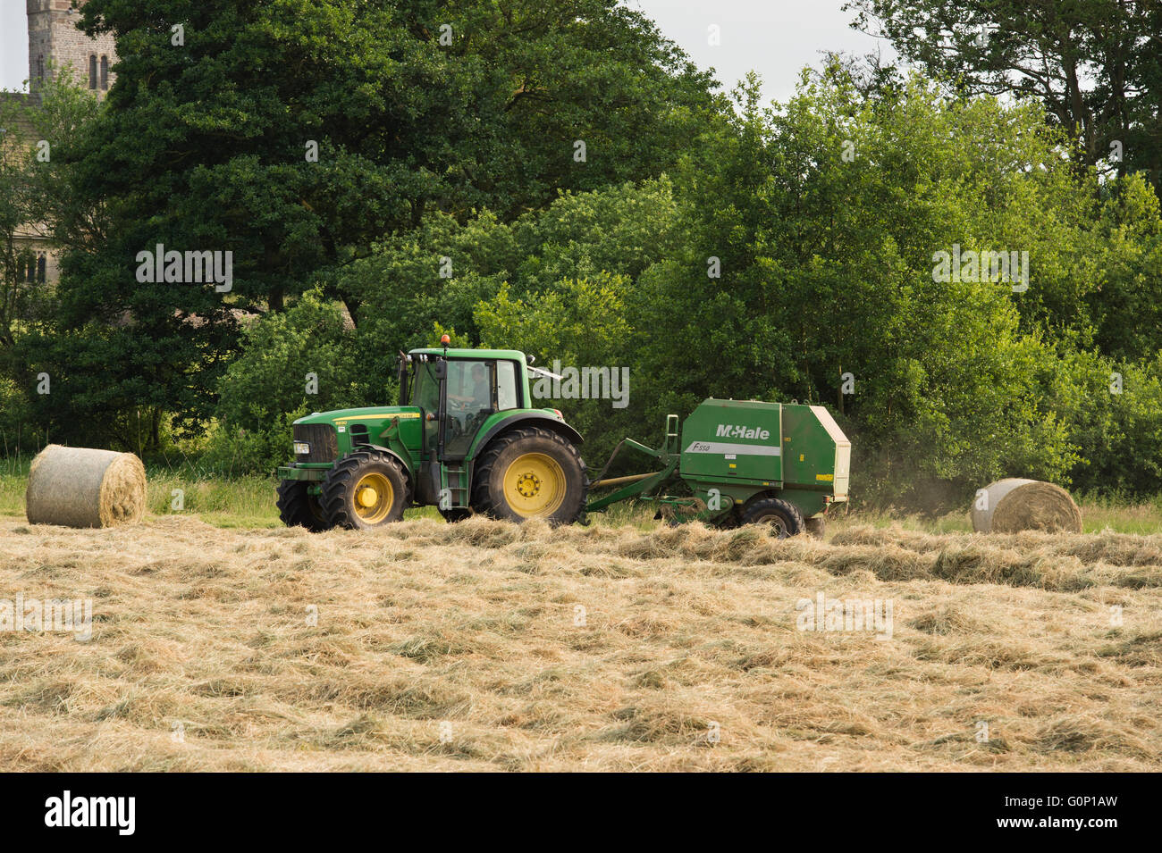 L'ensilage ou le foin de décisions - l'homme est le moteur du tracteur agricole vert tirant une ramasseuse-presse, travaillant dans un domaine - Grande Ouseburn, North Yorkshire, Angleterre, Royaume-Uni. Banque D'Images