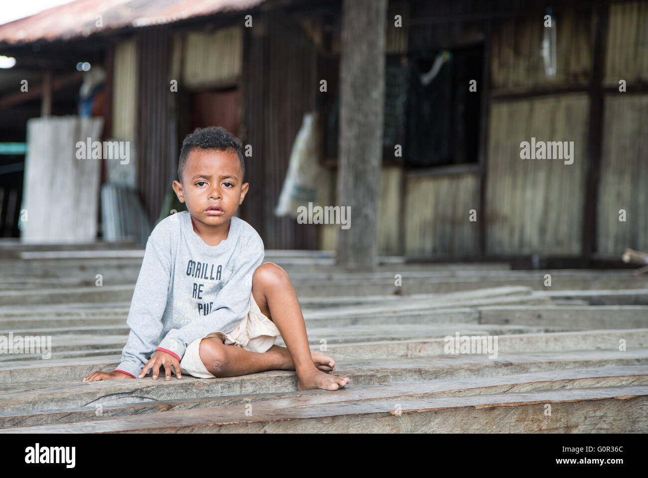 JAYAPURA, en Papouasie occidentale, INDONÉSIE - CIRCA FÉVRIER 2016 : petit garçon Papoue, à la malade et triste, assis Banque D'Images