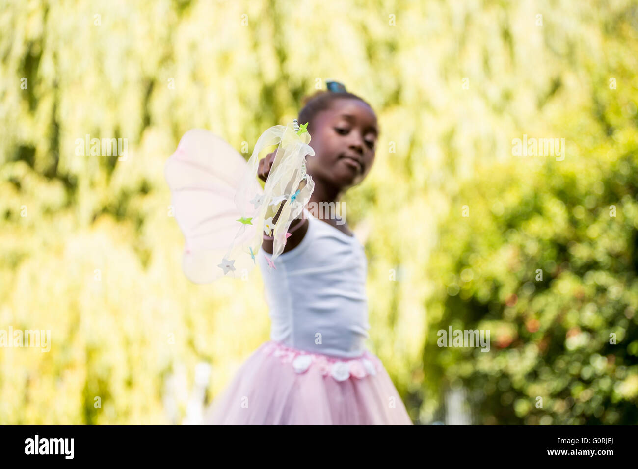 Cute girl de race mixte portant une robe de fée et orienter l'appareil photo avec sa baguette magique Banque D'Images