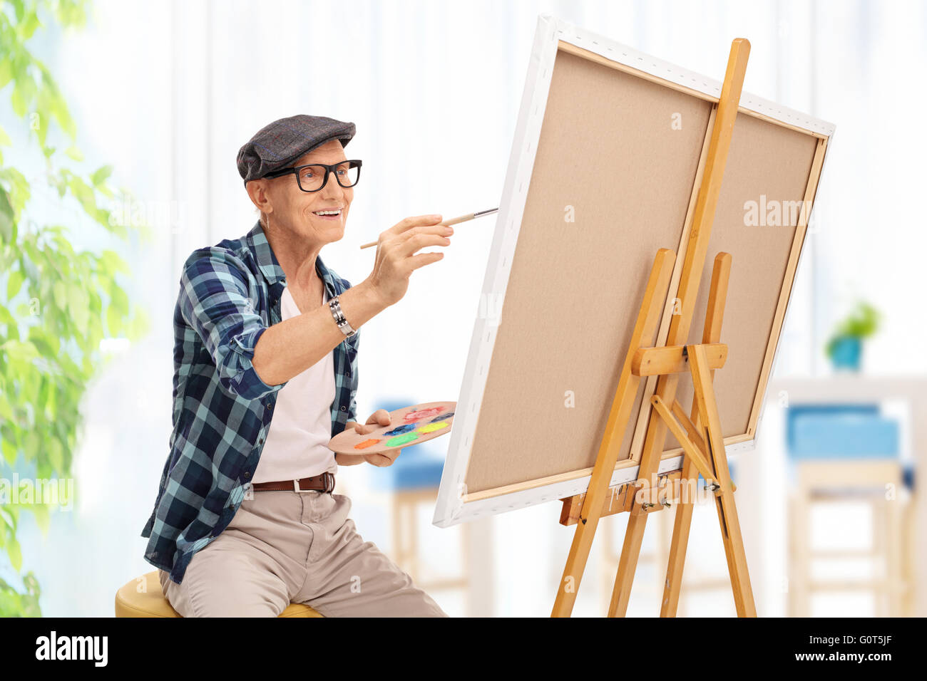 Un homme âgé s'appuyant sur une toile avec un pinceau à la maison Banque D'Images