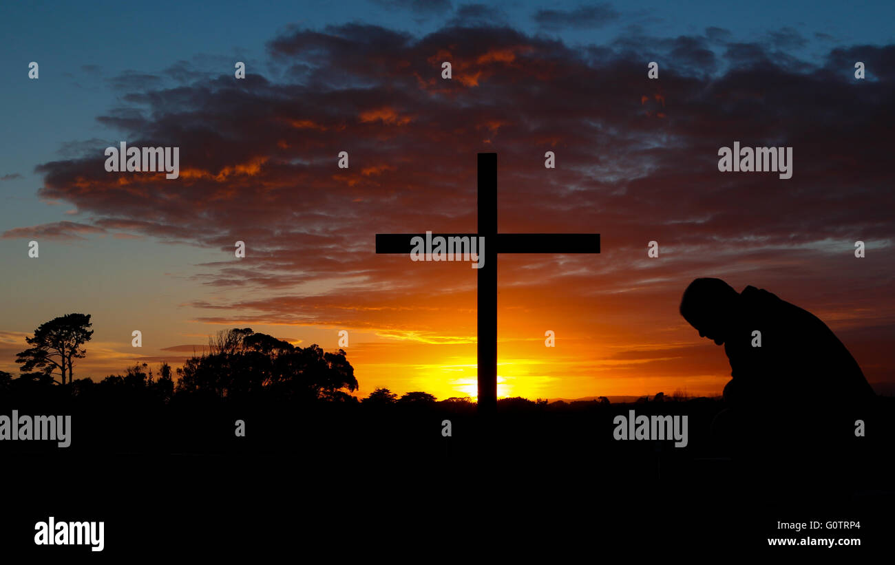 L'homme à prier devant une croix au lever du soleil. Banque D'Images