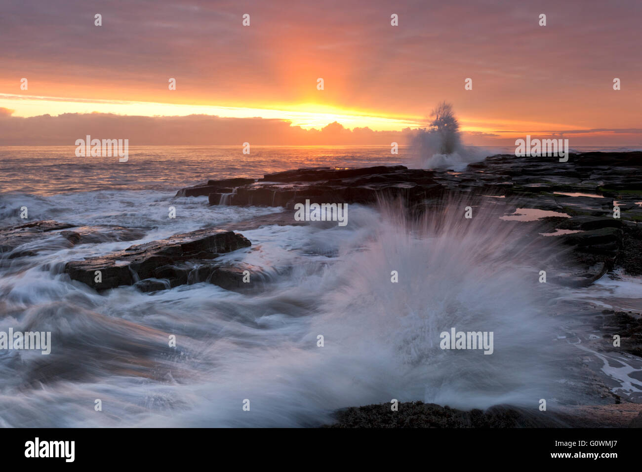 Vagues se brisant sur les rochers à Beacon Point par la mer sur Newbiggin le littoral nord-est au lever du soleil. Banque D'Images