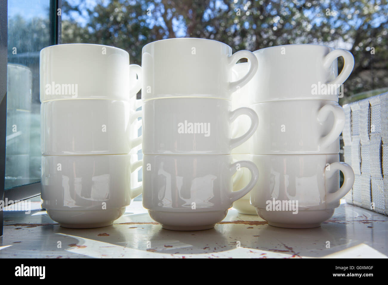 White tasses pour café et thé empilés sur la table vintage près de fenêtre ouverte sur le jardin Banque D'Images