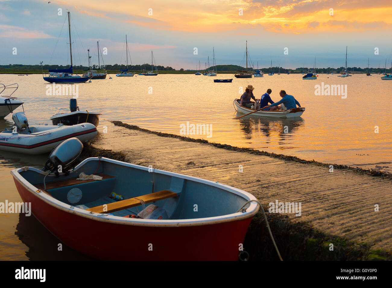 Bateau à rames personnes coucher du soleil, voir des gens dans une barque près de la jetée en bois sur la rivière Deben de Waldringfield, Suffolk, Angleterre. Banque D'Images