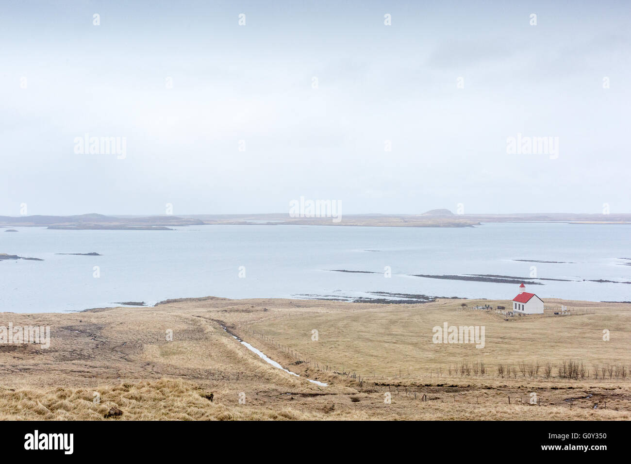 Une église blanche avec un toit rouge dans la distance de ce paysage islandais par l'eau. Banque D'Images