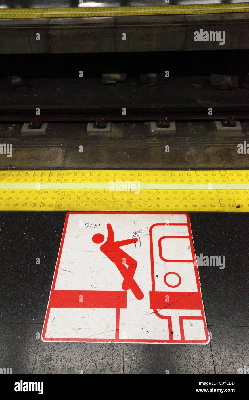 Graffitis artiste avec spray peut graffitis à l'esprit le signe d'avertissement d'écart et l'avertissement de bord tactile sur la plate-forme, station de métro Carabanchel, Madrid, Espagne Banque D'Images