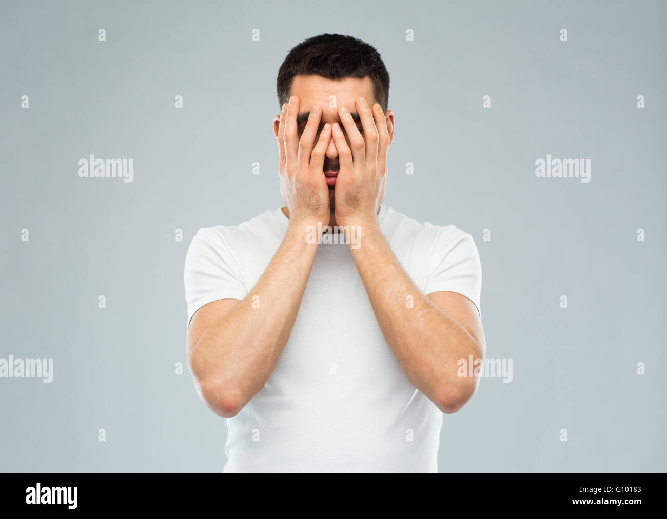 Homme en blanc T-shirt couvrant son visage avec les mains Banque D'Images