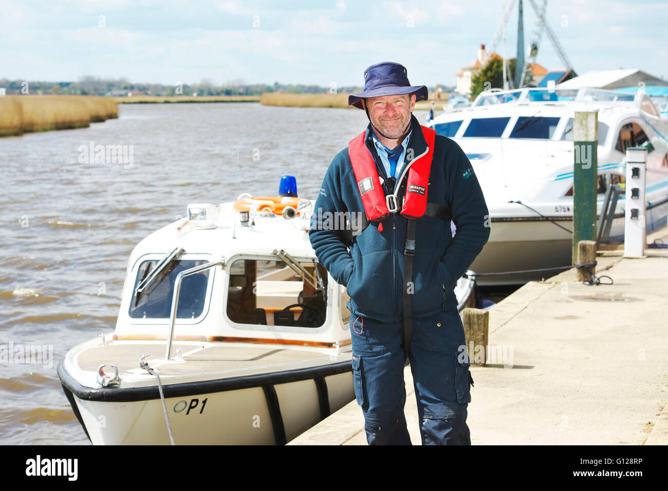 Broads Authority Ranger et officier de navigation posant au bord de la rivière près de son lancement de la police sur les Norfolk Broads Banque D'Images