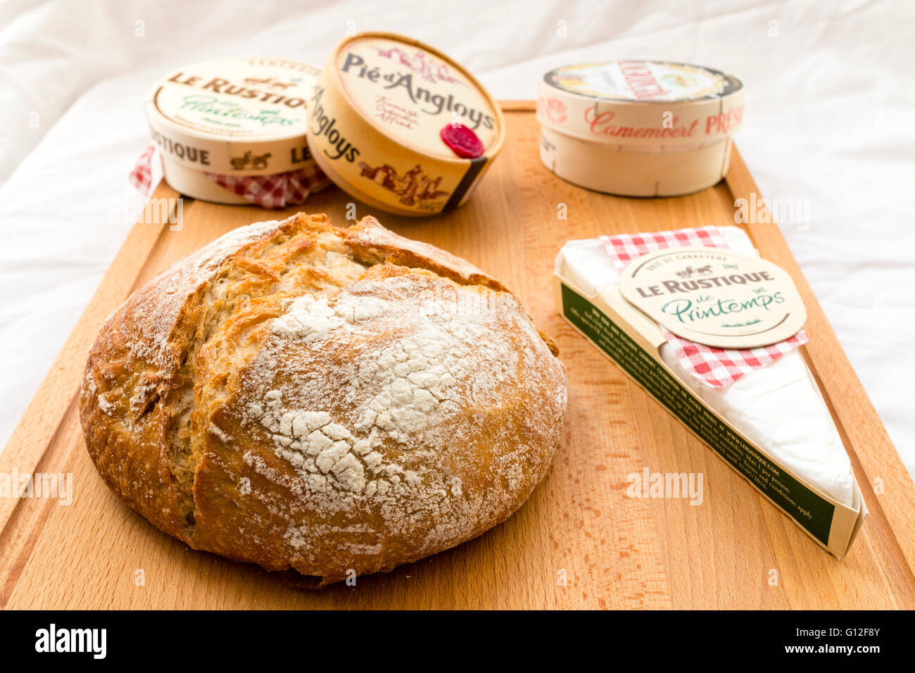 Les fromages français, en boîte et emballé, sur planche en bois rond avec du pain au levain pain. Camembert, Brie, diverses marques. Fond tissu blanc. Banque D'Images