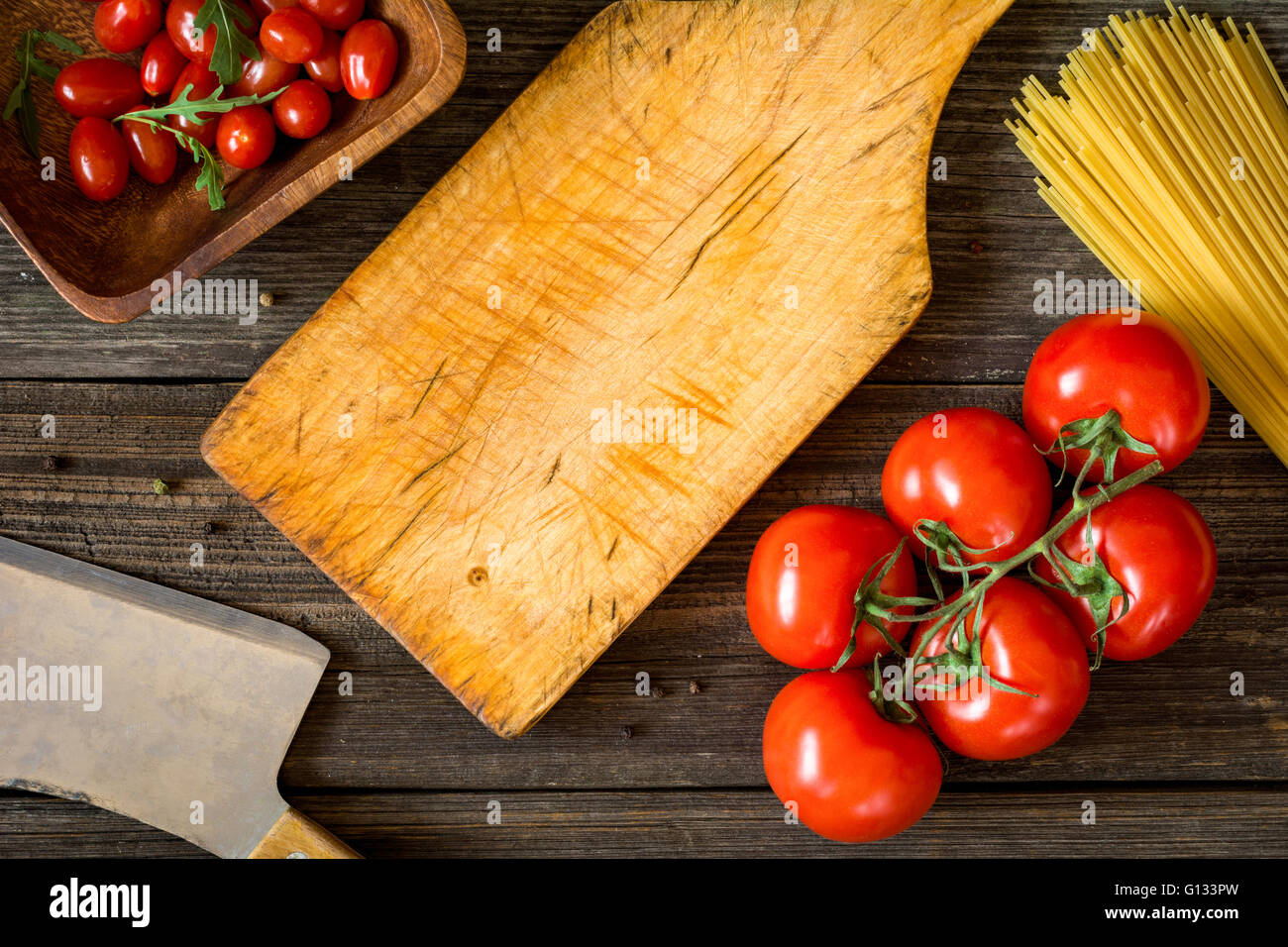 Vue de dessus de la nourriture de la cuisine italienne ingrédients sur toile rustique en bois. Les pâtes spaghetti, tomates, huile d'olive et salade de roquette Banque D'Images