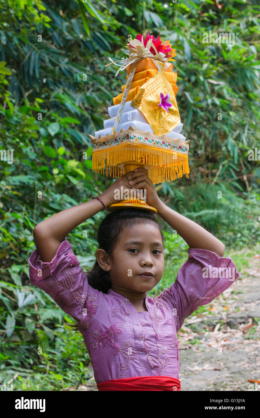 Une fille sur le chemin vers le temple avec des offres pour une cérémonie sur la tête, Bali, Indonésie Banque D'Images