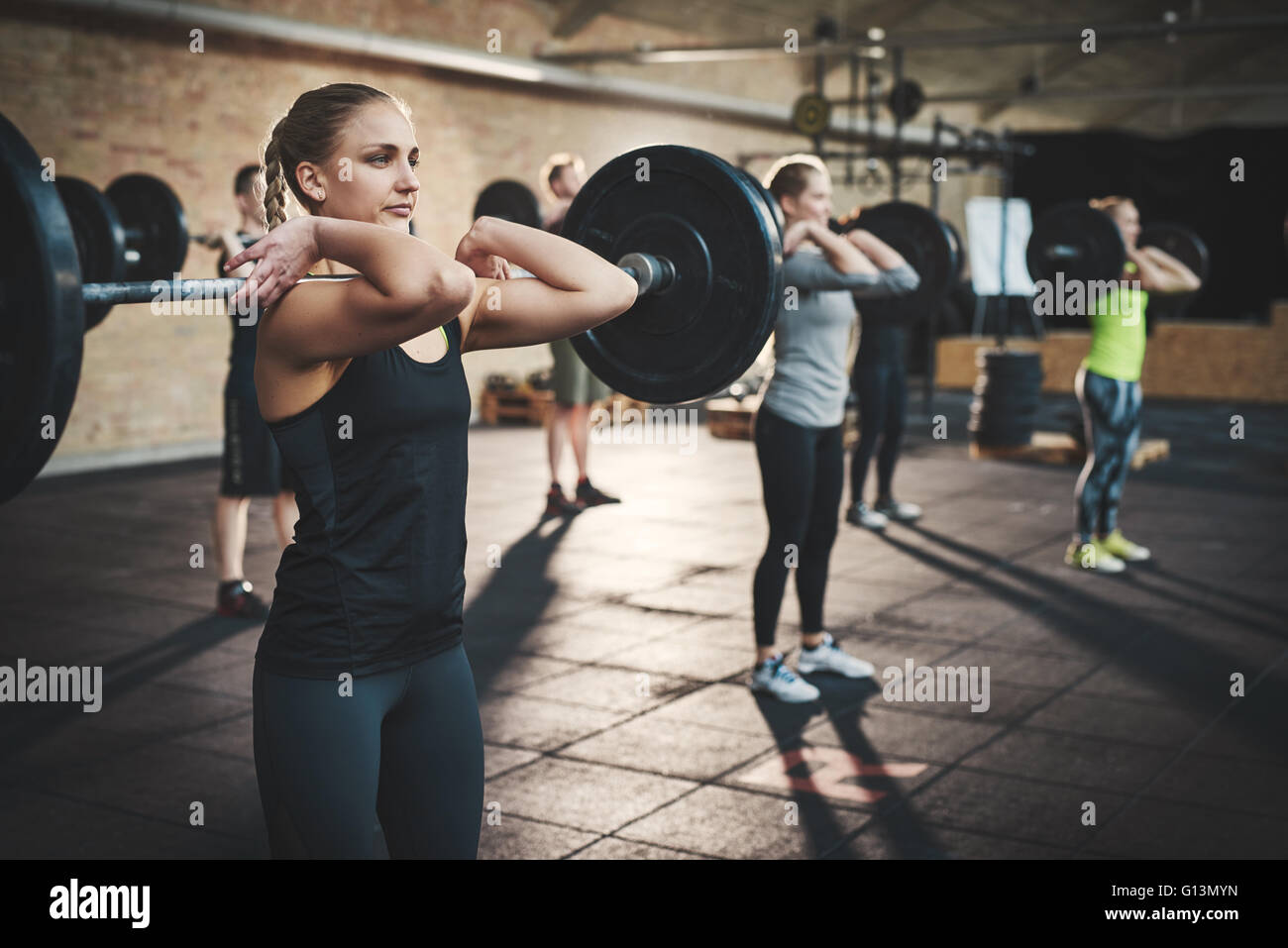 Fit young woman lifting des barres à l'accent, s'entraîner dans un gymnase avec d'autres personnes Banque D'Images