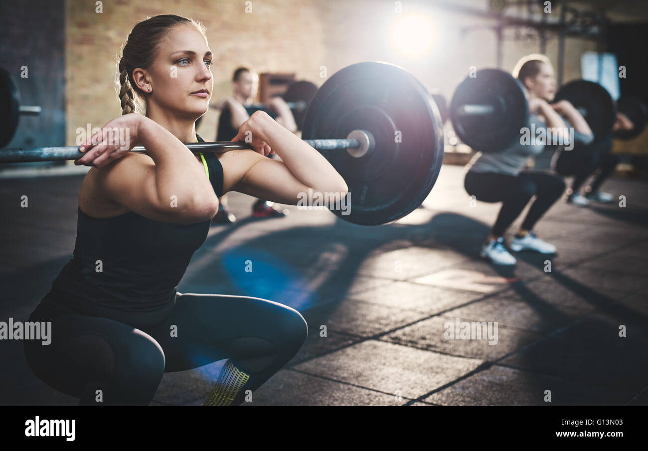 Fit young woman lifting des barres à l'accent, s'entraîner dans un gymnase avec d'autres personnes Banque D'Images