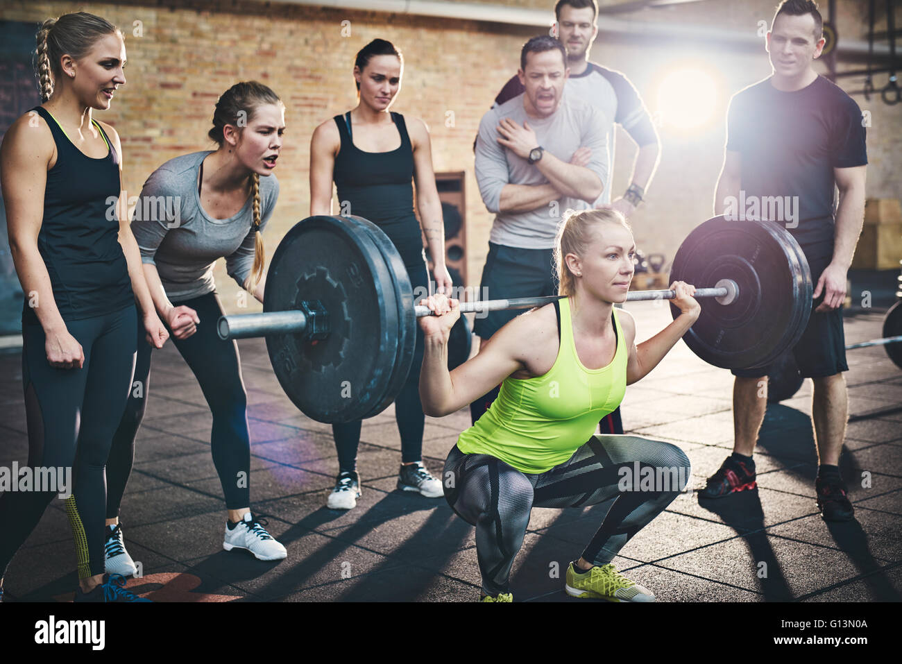 Fit young woman lifting des barres à l'accent, s'entraîner dans un gymnase avec d'autres personnes sur son encouragement Banque D'Images