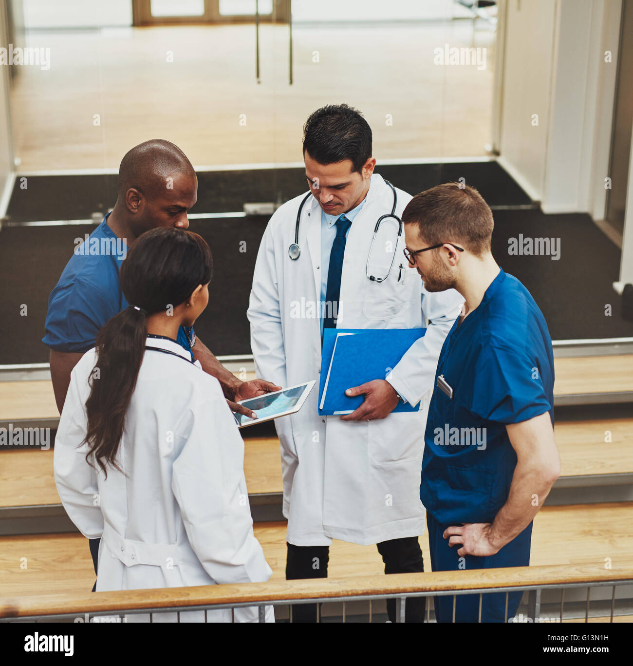 Groupe multiracial de médecins dans une réunion impromptue debout sur un escalier à la recherche de l'information sur un ordinateur tablette, voir f Banque D'Images