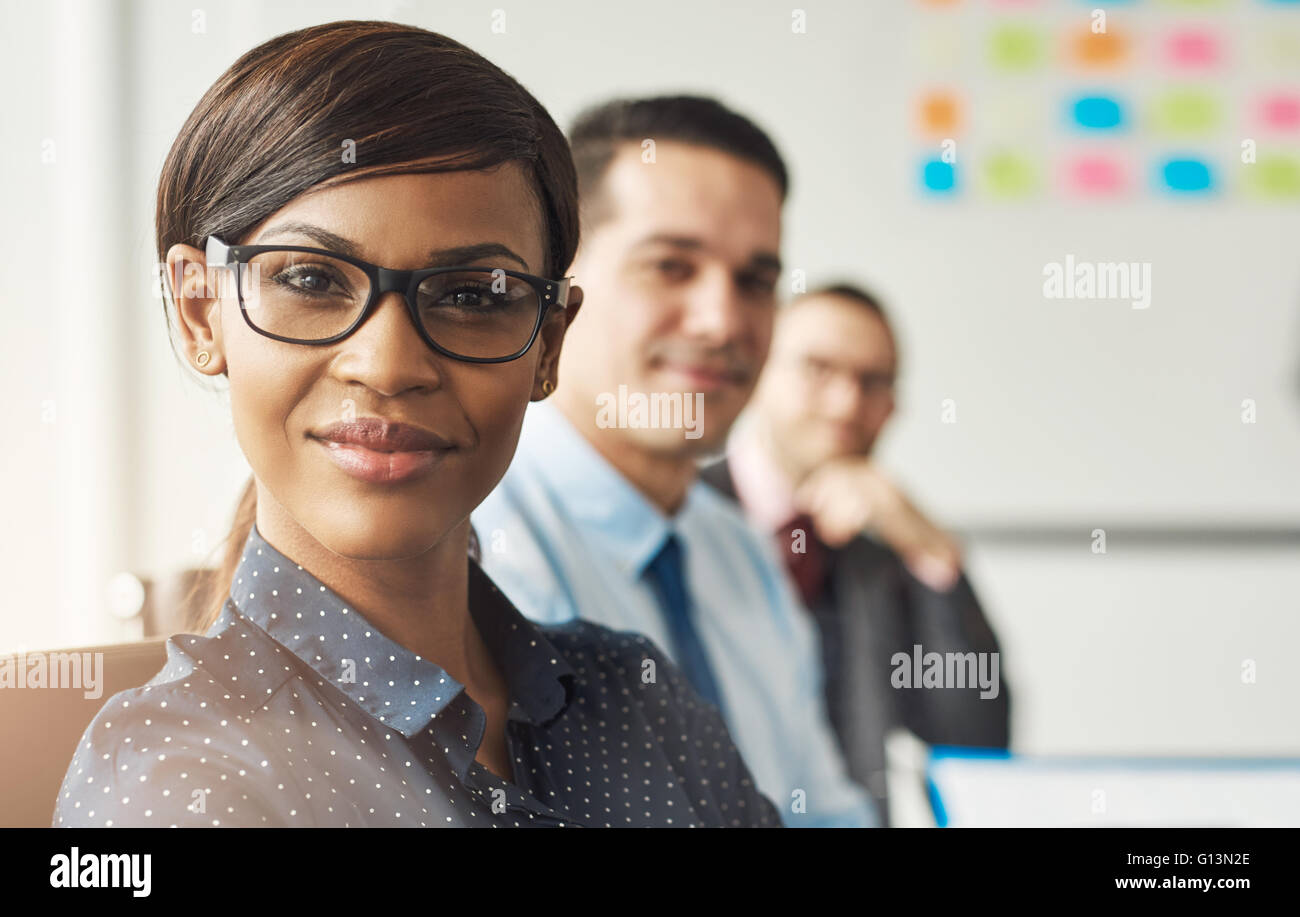 Beautiful smiling business woman wearing eyeglasses et blanc polka dotted shirt assis avec leurs collègues masculins au travail Banque D'Images