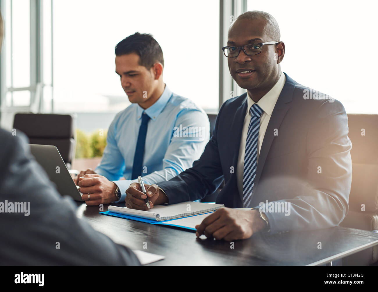 Beau Black souriant propriétaire d'affaires exécutif, assis à table avec des employés avec le bloc-notes en face de lui Banque D'Images