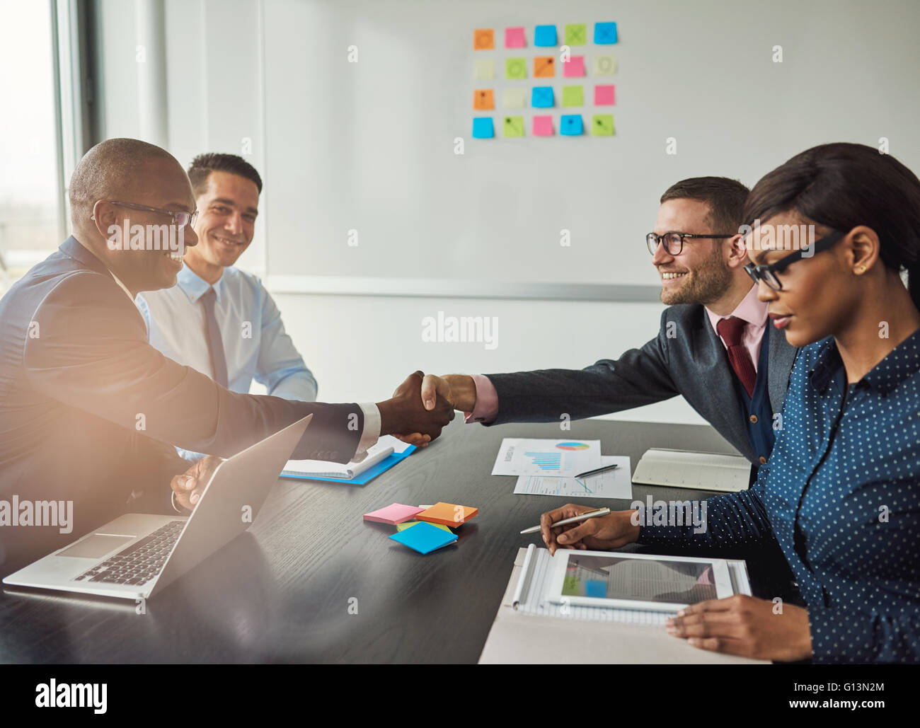 De l'équipe multiraciale, la conclusion d'un accord d'entreprise d'atteindre à travers la table pour serrer la main de sourires heureux avec l'accent d'un yo Banque D'Images