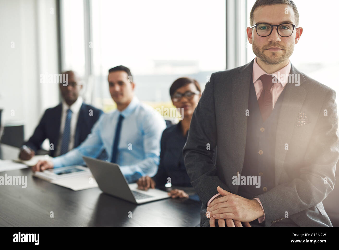 Handsome Young executive avec trois employés assis sur table edge avec retour à la grande fenêtre de bureau lumineux avec lumière flare Banque D'Images