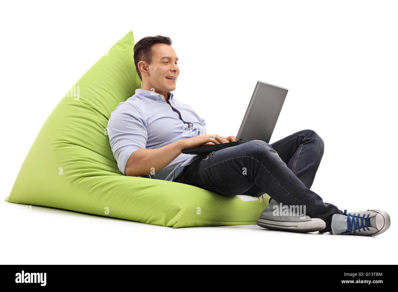 Cheerful man working on laptop assis sur un pouf vert isolé sur fond blanc Banque D'Images